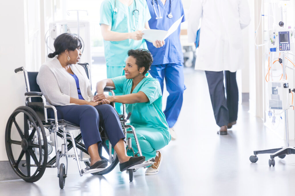 Nurse providing support to a patient in a wheelchair in a hospital hallway, representing compassionate healthcare and patient care in a clinical setting.