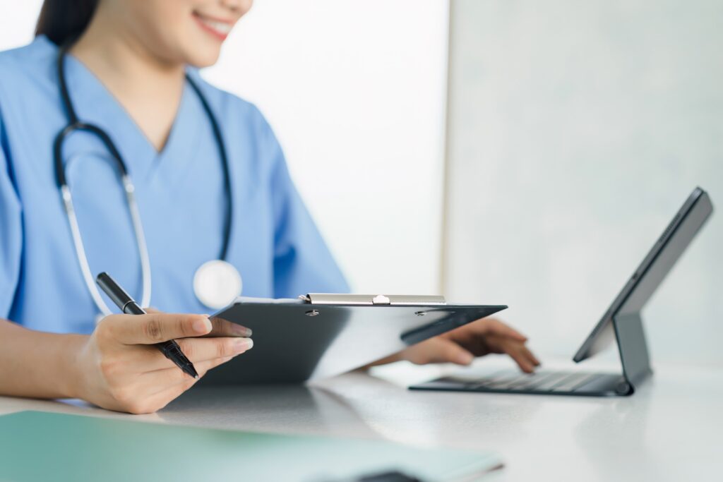 Healthcare professional reviewing patient management software on a tablet while writing notes, illustrating the integration of technology to streamline administrative tasks in medical practice.